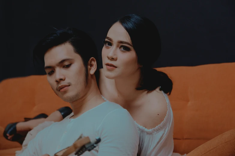 two people sitting on top of an orange couch