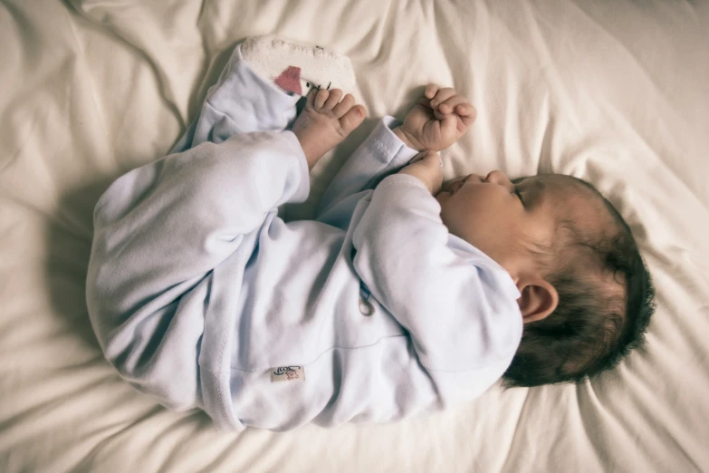 an infant laying on a bed wearing a blue outfit