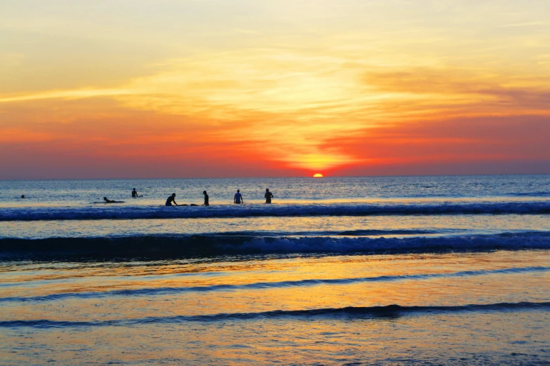 group of people at the water's edge with surfboards as sun sets