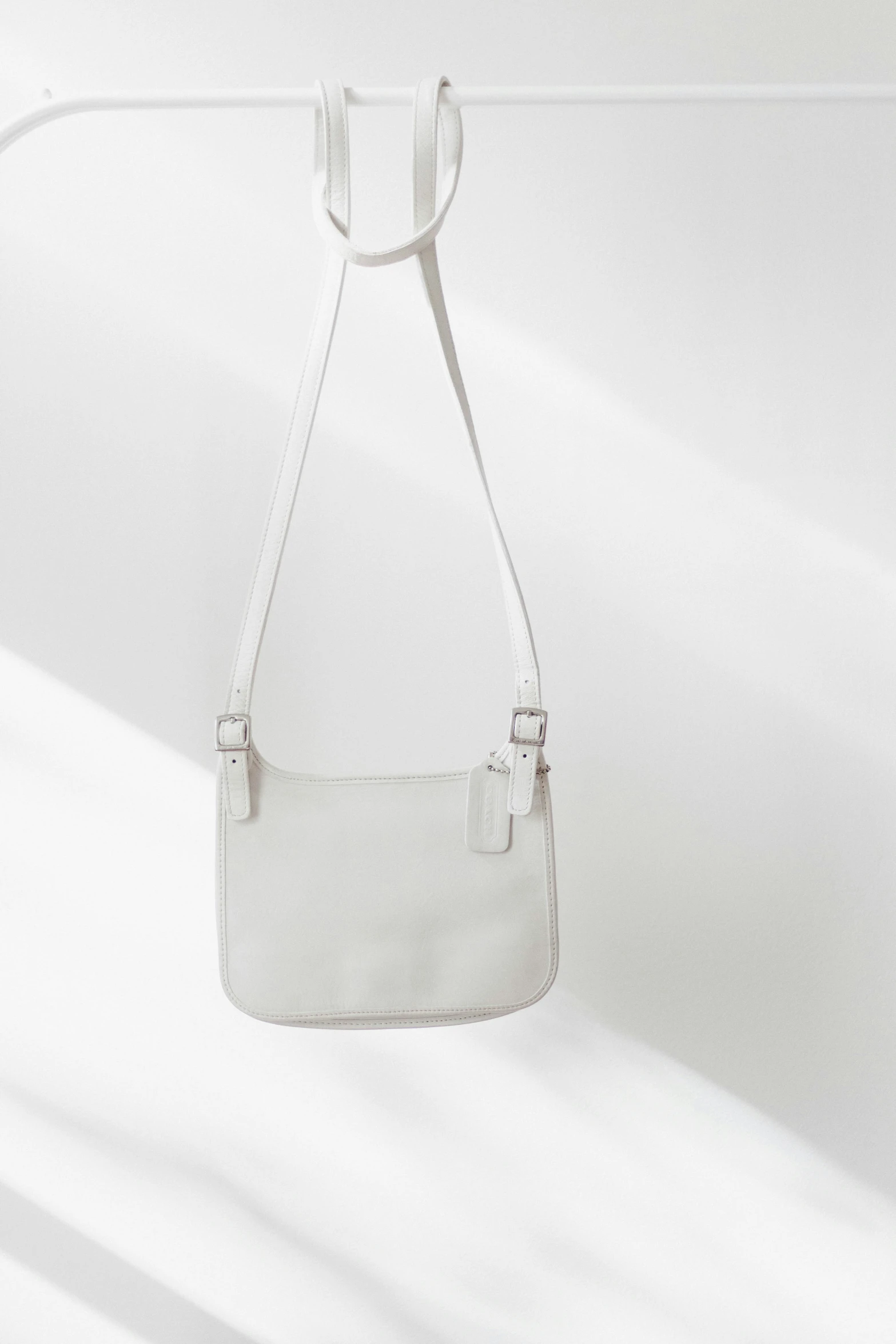 the front side of an off - white leather bag hanging on a hook with two handles