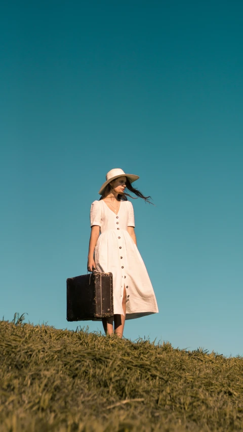 a woman wearing a hat and dress holds a briefcase