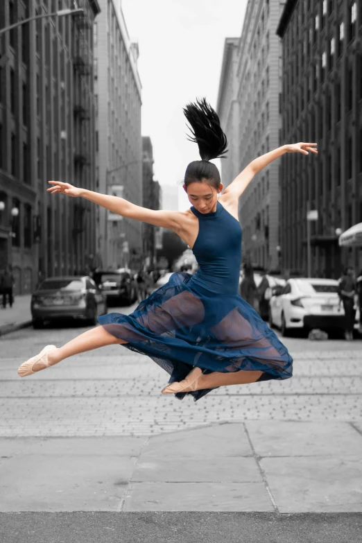 a woman in a blue dress jumping with her legs stretched out