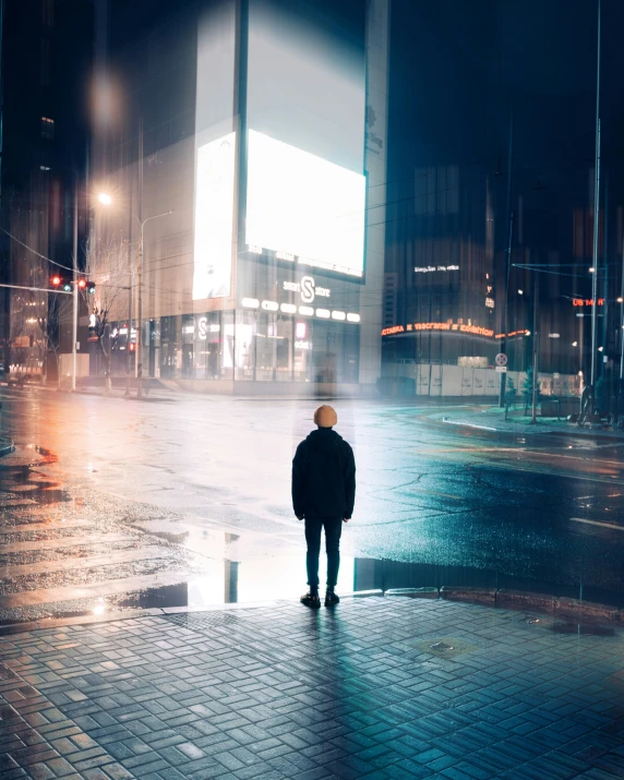 man standing on sidewalk at night near city street