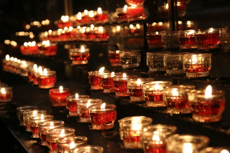 several rows of lit candles sit on a black surface