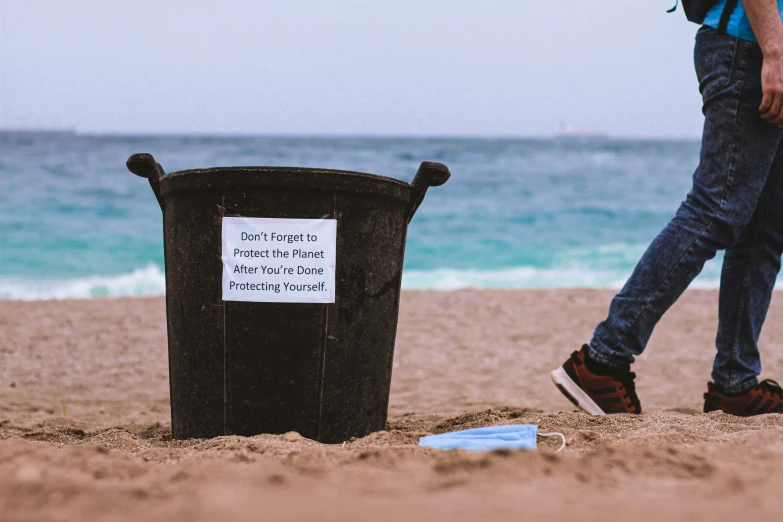 a person walking by a trash can on the beach