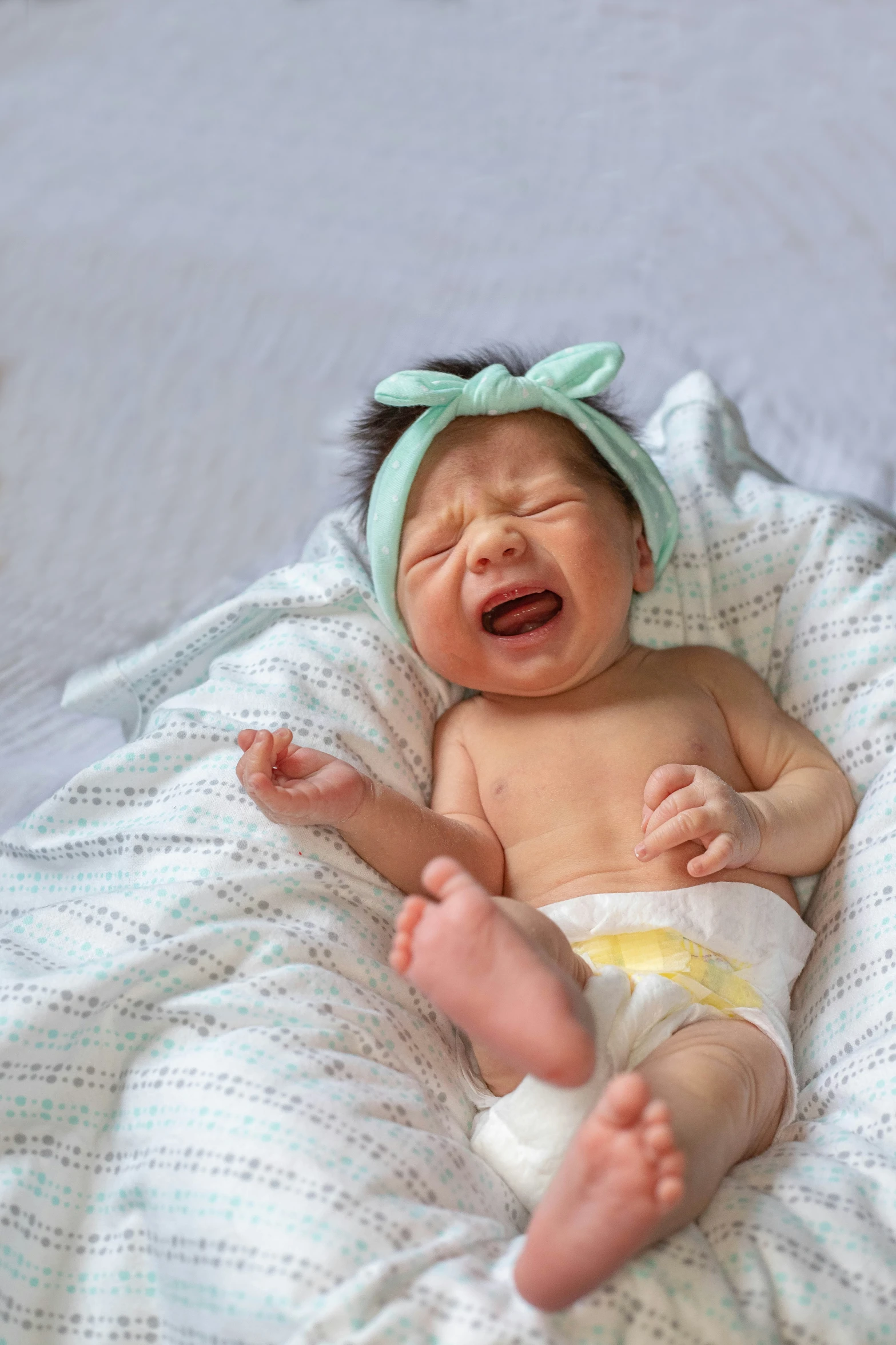 a crying newborn baby laying on a white sheet