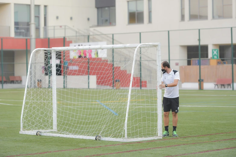 man standing in front of a soccer goal with his cell phone