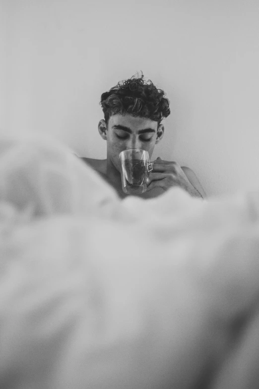 a man laying in bed with his eyes closed drinking from a glass
