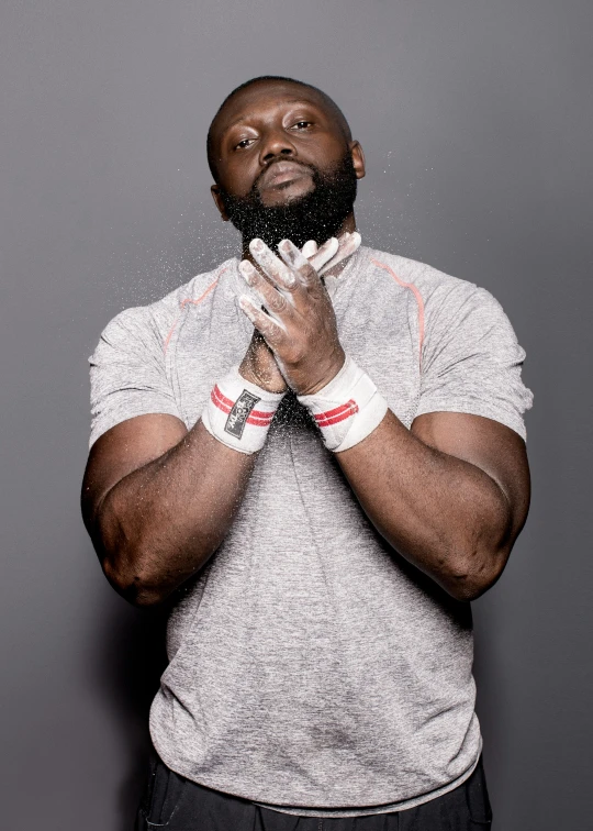 an african american man with a gray shirt, white wrist bands and his hands clasped, looking up into the camera while holding a napkin