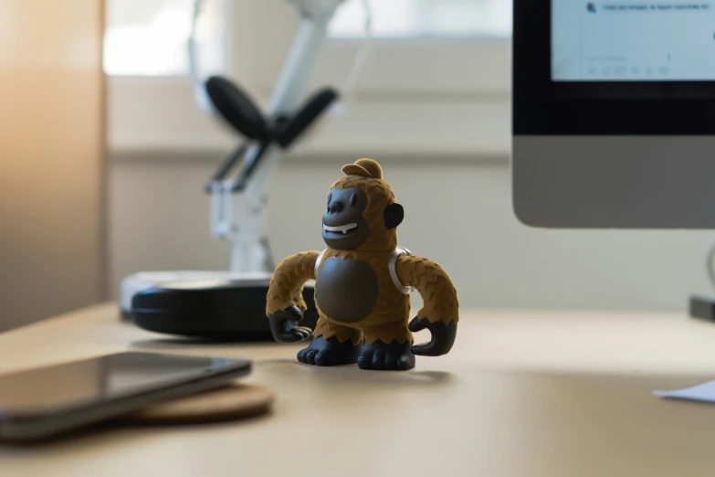 a toy monkey sits on a desk with a computer