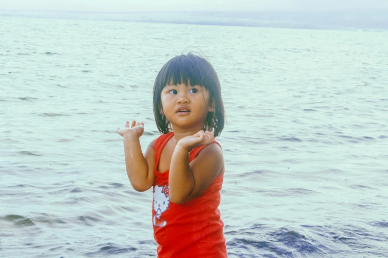 a small child standing near the water with her arm out and eyes wide open