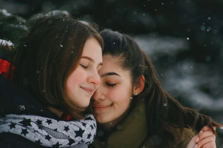 two girls hugging one another, snow falling in the background