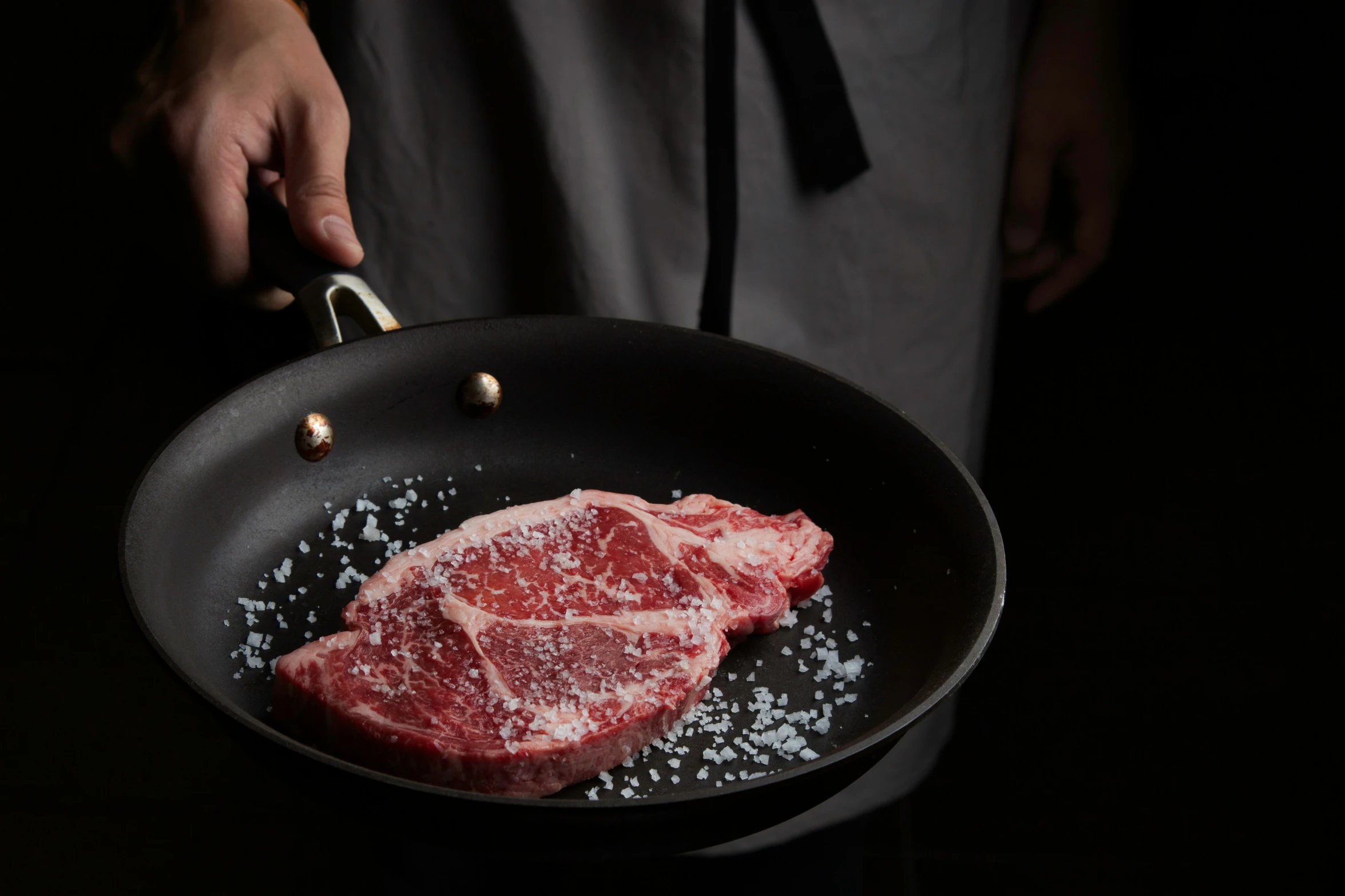 raw raw steak in a frying pan being held up by a hand