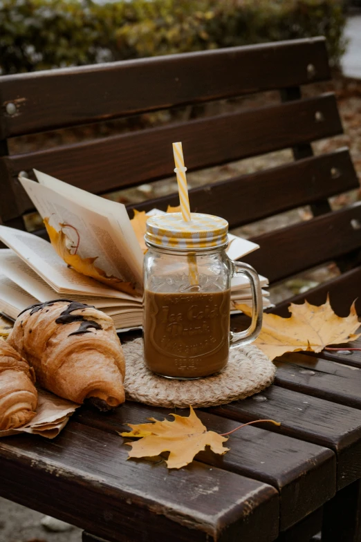 two croissants are laying on a table with an open book and a glass jar