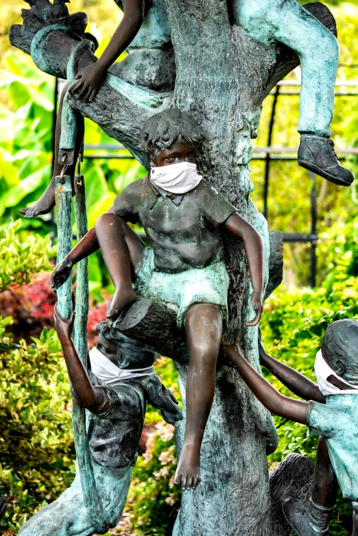 a tree is covered in statues that include people wearing surgical masks