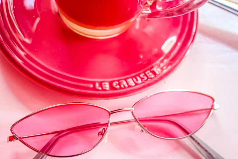 pink and gold sunglasses sitting on the ground next to a cup