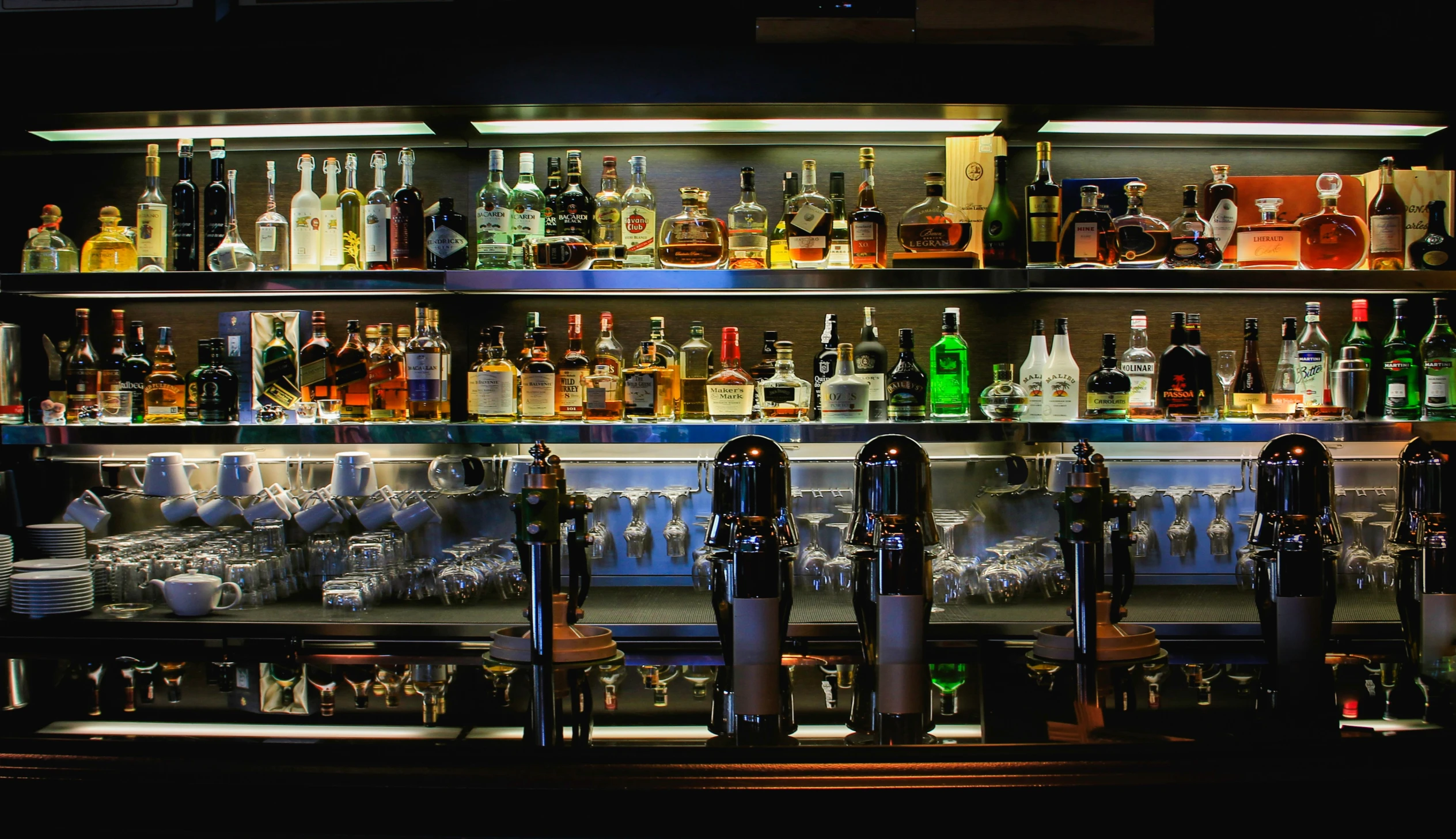 shelves of liquor bottles are filled with glasses