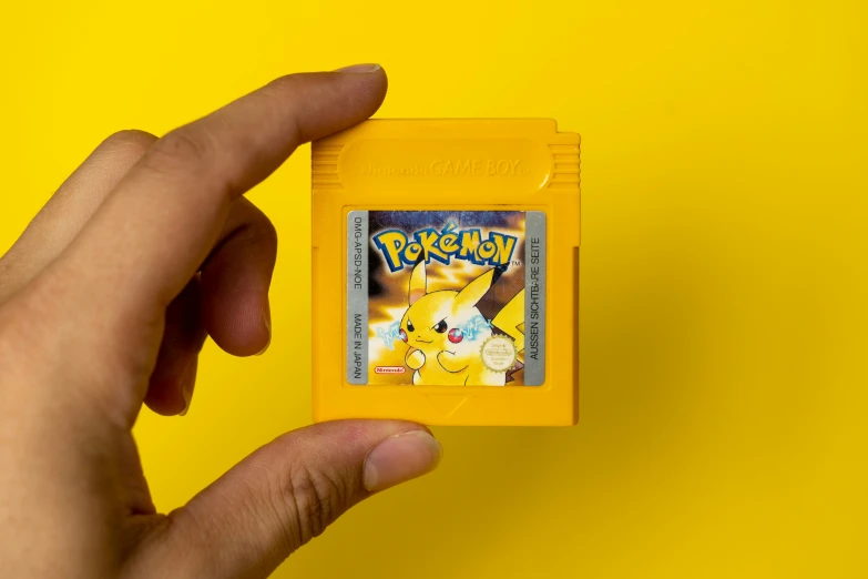 a man holding a yellow pokemon gameboy with a yellow back ground