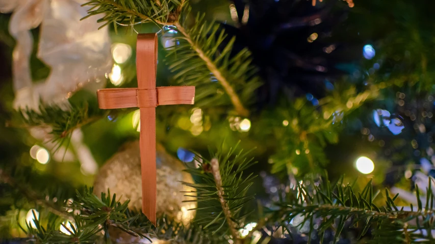 a cross on a wooden stick hangs from the christmas tree