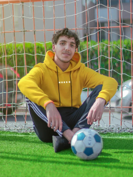 a young man is sitting in the grass with a soccer ball