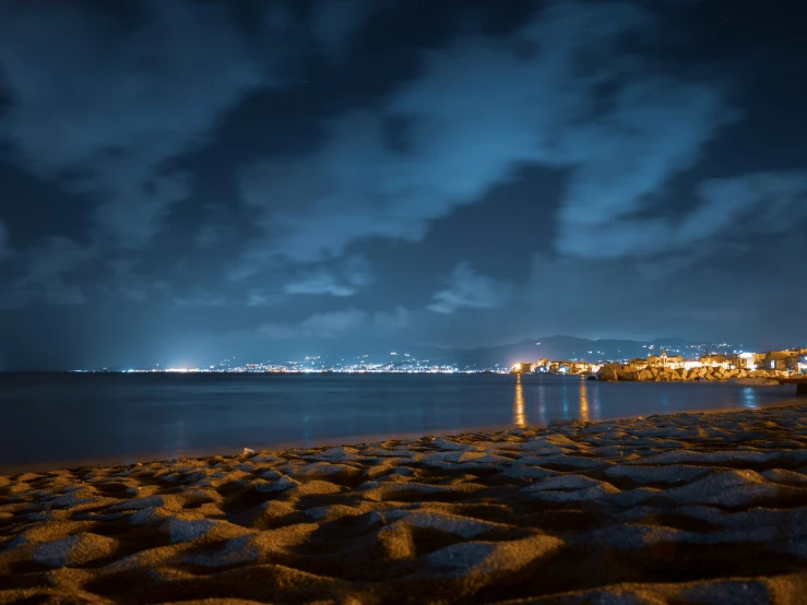 an ocean at night with buildings on the horizon and some clouds in the sky