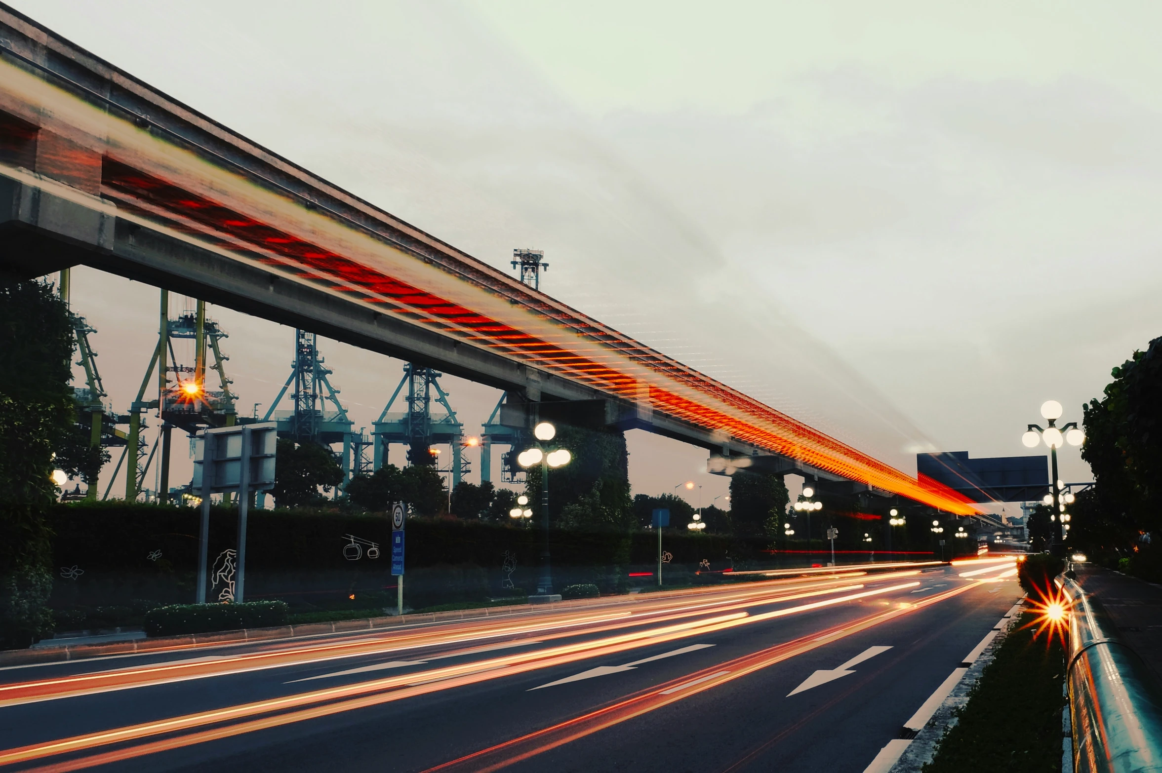 a road with several cars coming towards the camera and going under a long bridge