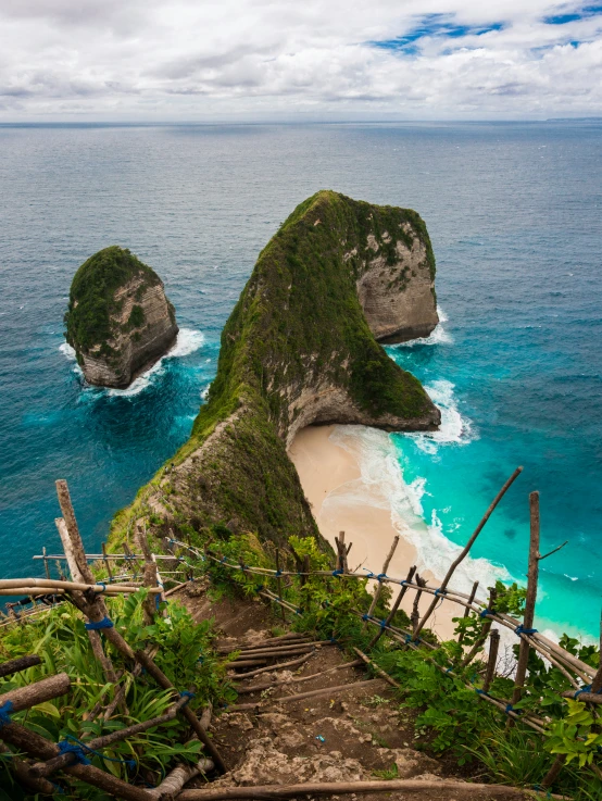 a rock formation sitting next to a beach under a cloudy blue sky