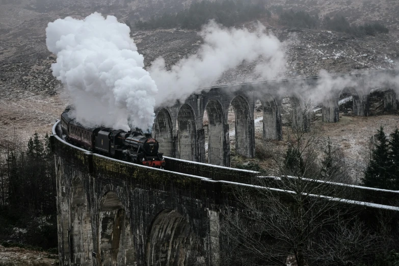 a steam train rides down the tracks next to stone structures