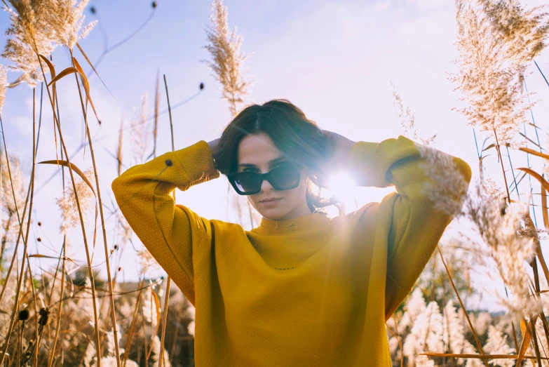 a woman wearing sunglasses and a sweater standing near tall grass