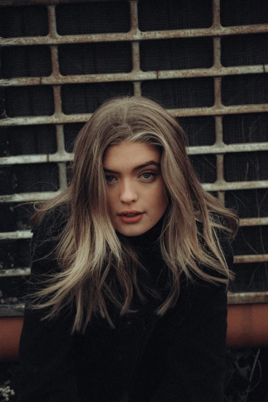 a young woman is sitting against a wall wearing a sweater