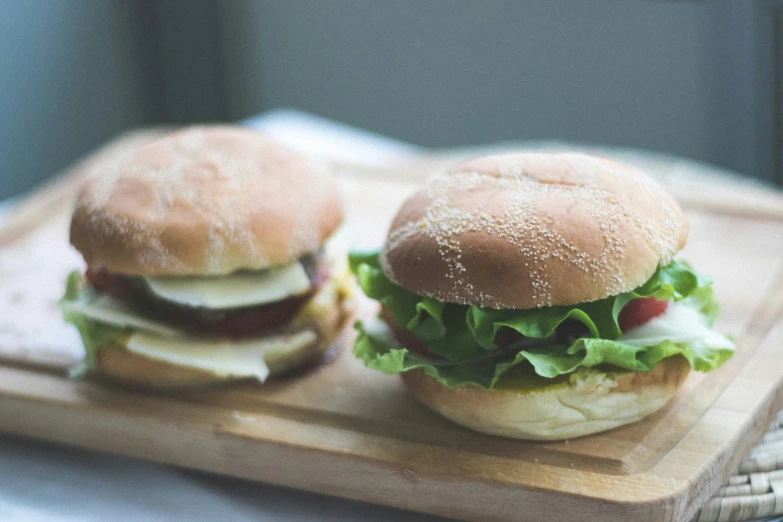 two hamburgers are on a board next to each other