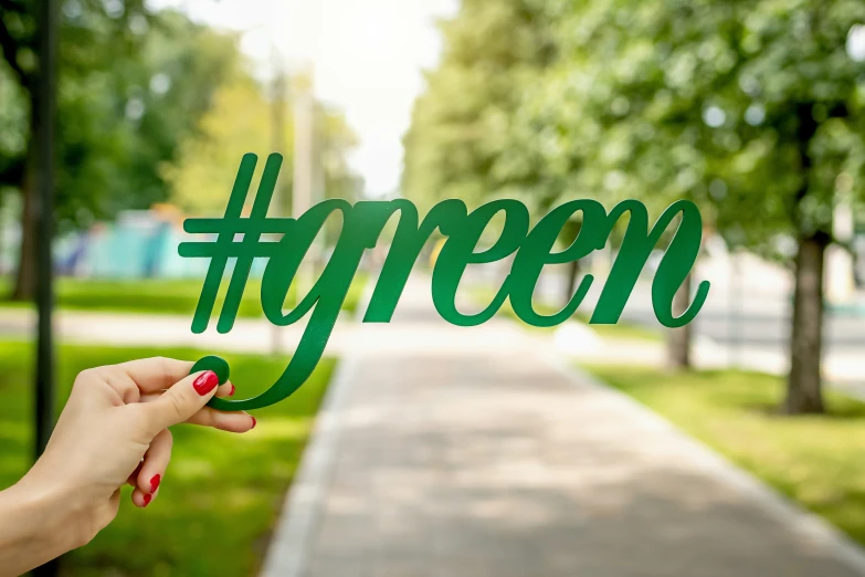 someone holding up the word green in front of a sidewalk