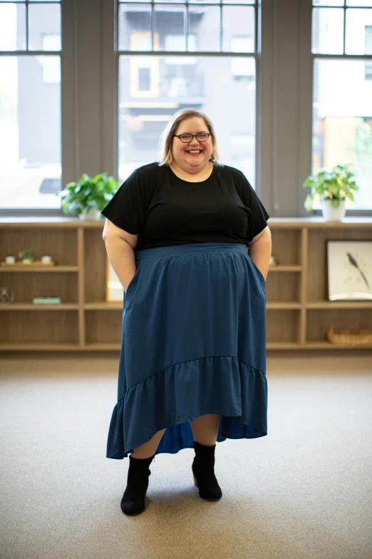 a smiling woman in a black shirt is standing next to a book shelf and large window