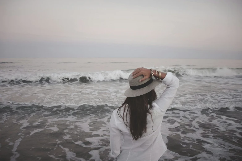 a woman holding a hat next to the ocean