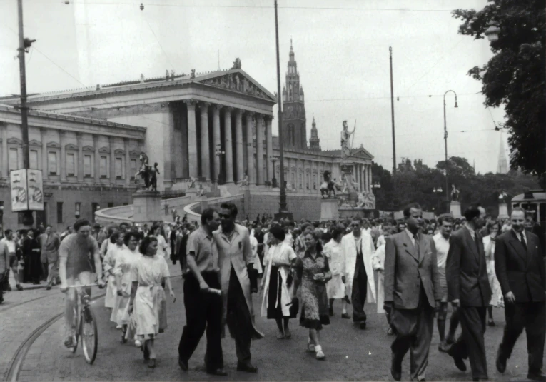 people walking and sitting on benches next to a building