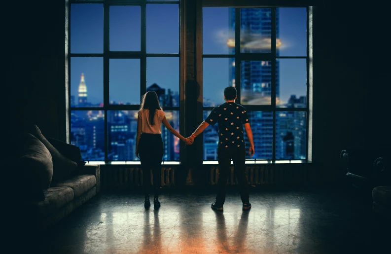 the two people are standing close to each other in front of a large window