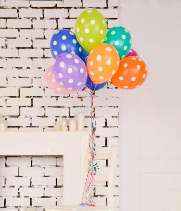 four colorful balloons in front of a white brick wall