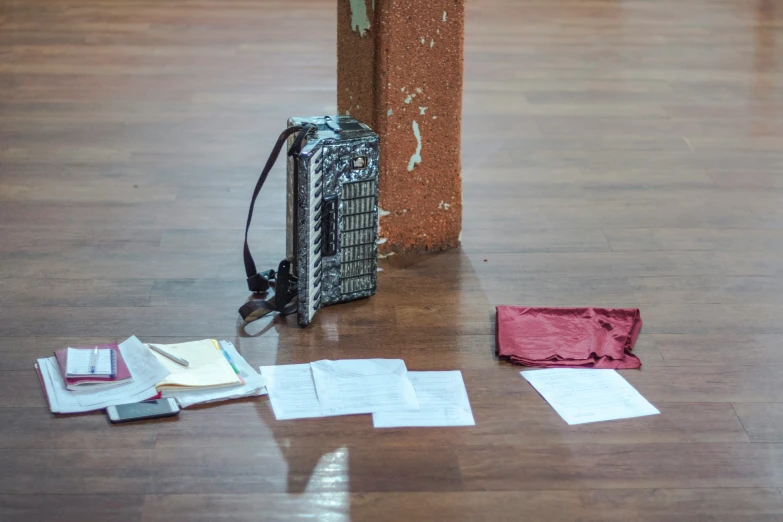 a red purse sitting on top of a wooden floor next to two pieces of paper