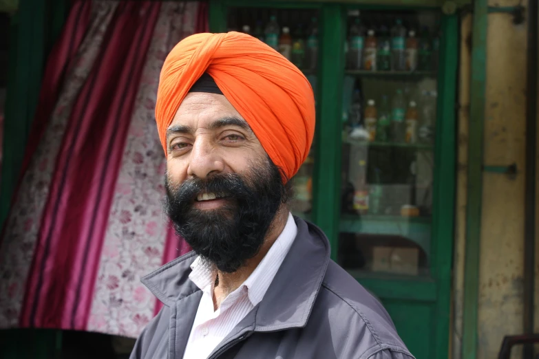 a man with an orange turban and beard posing in front of a green shop