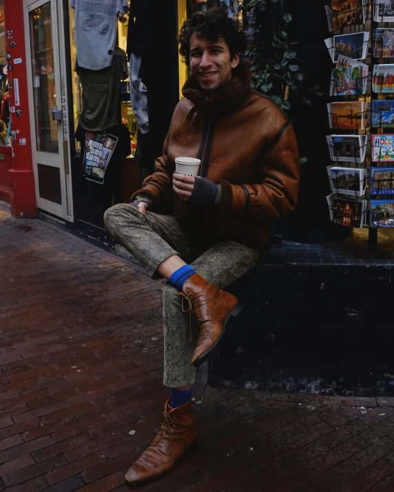a man sits outside in front of a store holding a cup of coffee