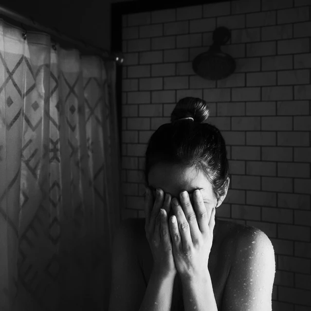 a black and white po of a woman covering her face in the bathroom