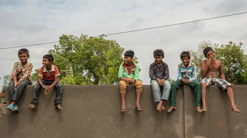 four boys sit on top of a stone wall