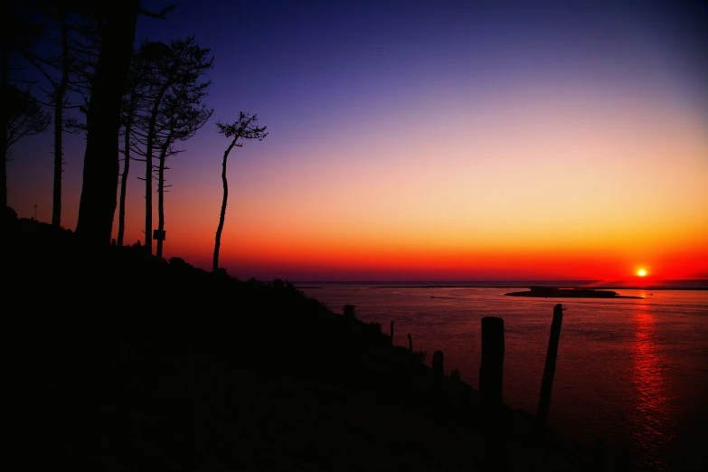 the sunset as seen from the edge of a hill near a body of water