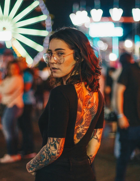 a woman wearing glasses and a tattoo standing in front of a wheel