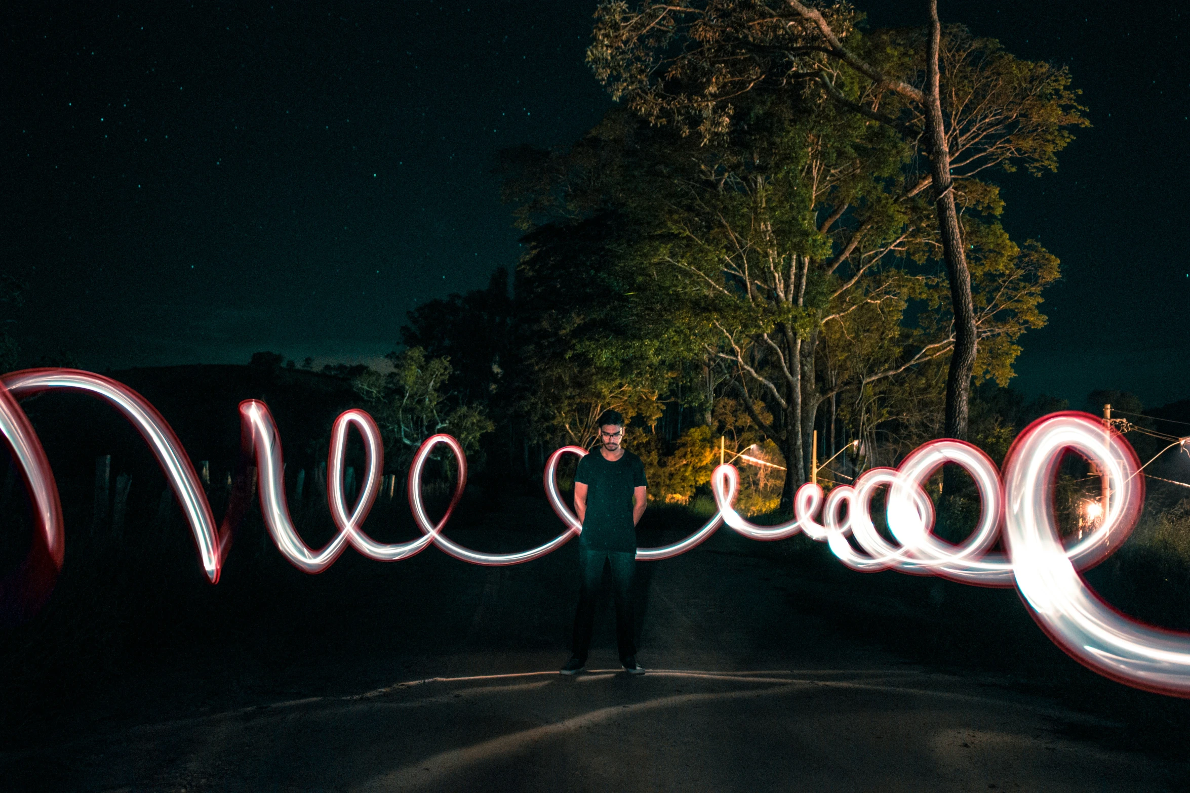 a man stands on a dark road next to light art