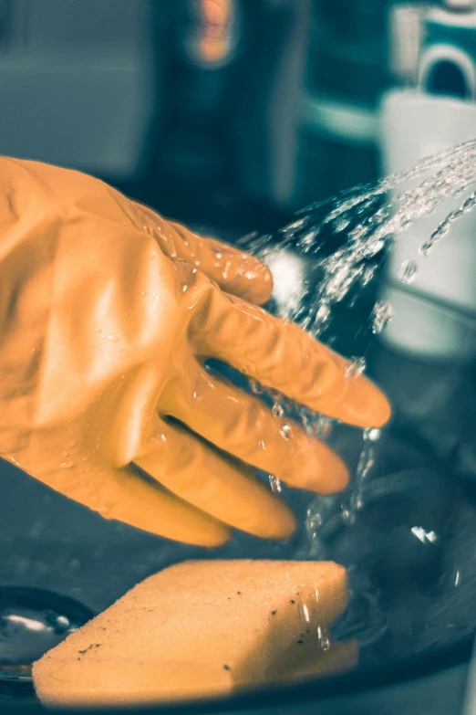 yellow gloved hands pouring water into small bowl of soapy substance