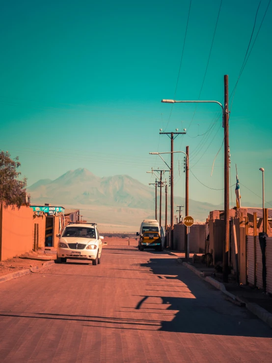 cars parked along a dirt road surrounded by hills and telephone poles