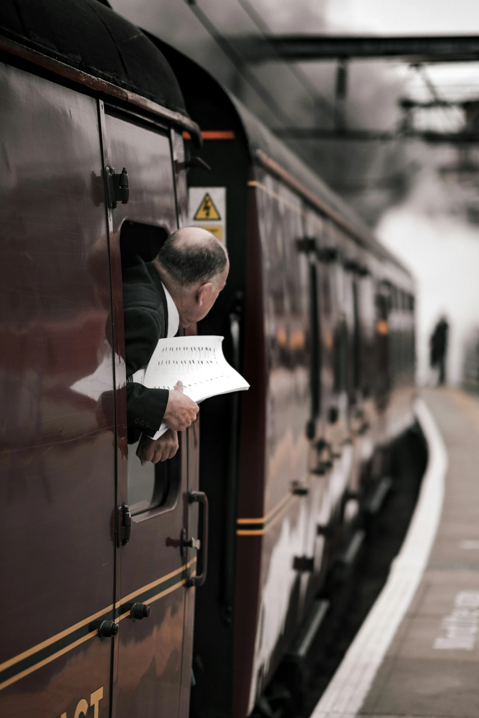 an older man with a sheet of paper leaning out of a train