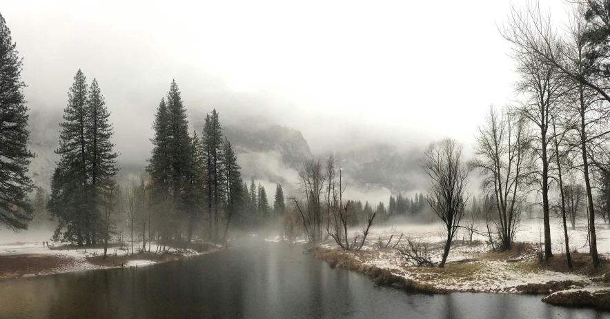 a lake is surrounded by snow, trees and fog