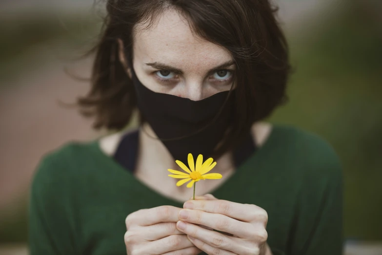 a woman wearing a black face mask holds a yellow flower